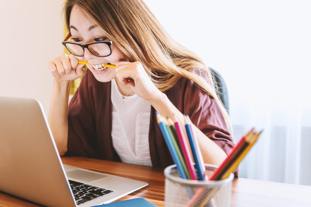 woman looking at laptop biting a pencil